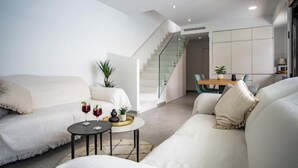 Una sala de estar moderna con un juego de sofá, una mesa de centro con bebidas y una escalera que conduce a un comedor.