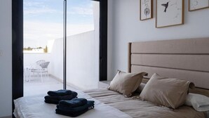 Et soveværelse med seng, puder, et foldet håndklæde og udsigt til en balkon.
