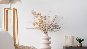 Et soveværelse med en seng, et natbord med lampe, en vase med tørrede blomster og en lille potteplante.