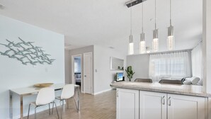 Eine moderne Küche mit weißen Schränken, ein Essbereich mit weißem Tisch und Stühlen sowie Pendelleuchten.