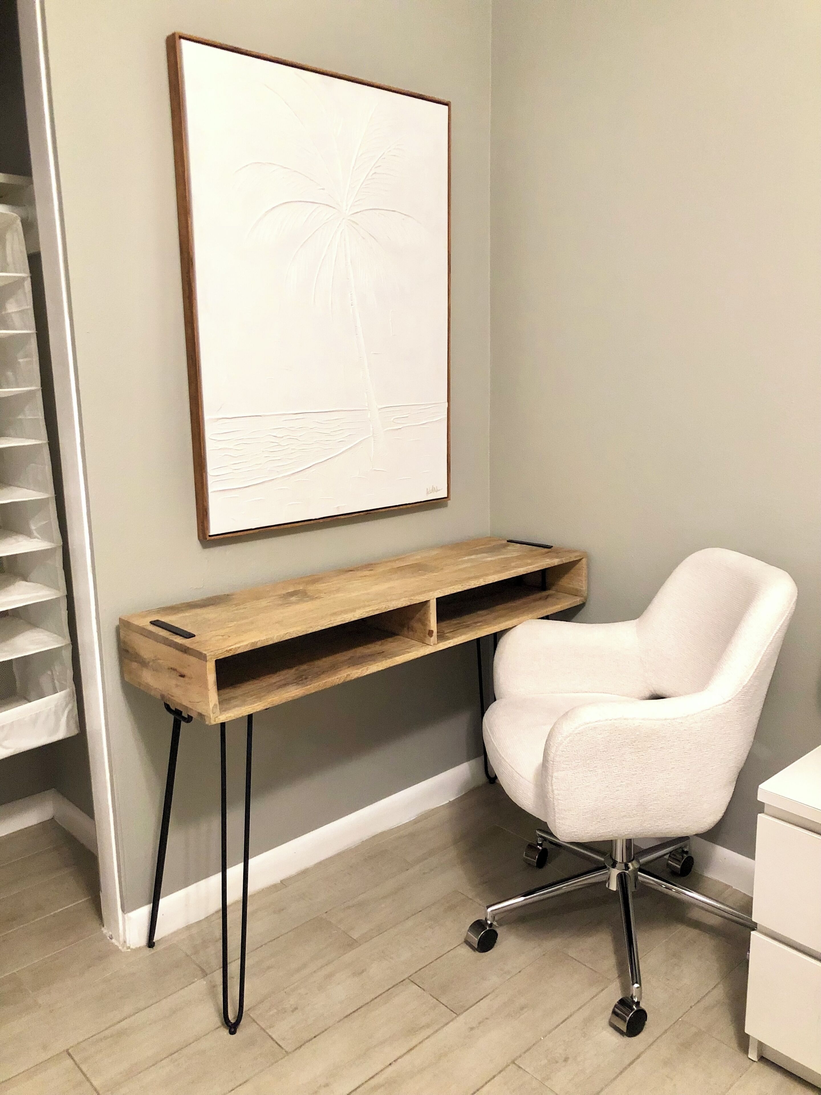 A room with a white office chair, a wooden desk, a framed artwork, and a white cabinet.