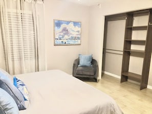 A bedroom with a bed, a chair, a wardrobe, and a painting on the wall. - Turn-Key 2BR Sarasota Oasis: Private Yard, Fully Stocked, Beaches & Downtown (Sarasota)