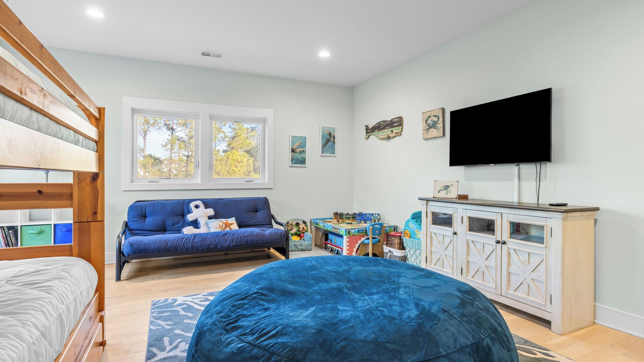 Habitació infantil amb llits superposats, un sofà blau, un seient de sac, una televisió i un armari de fusta.