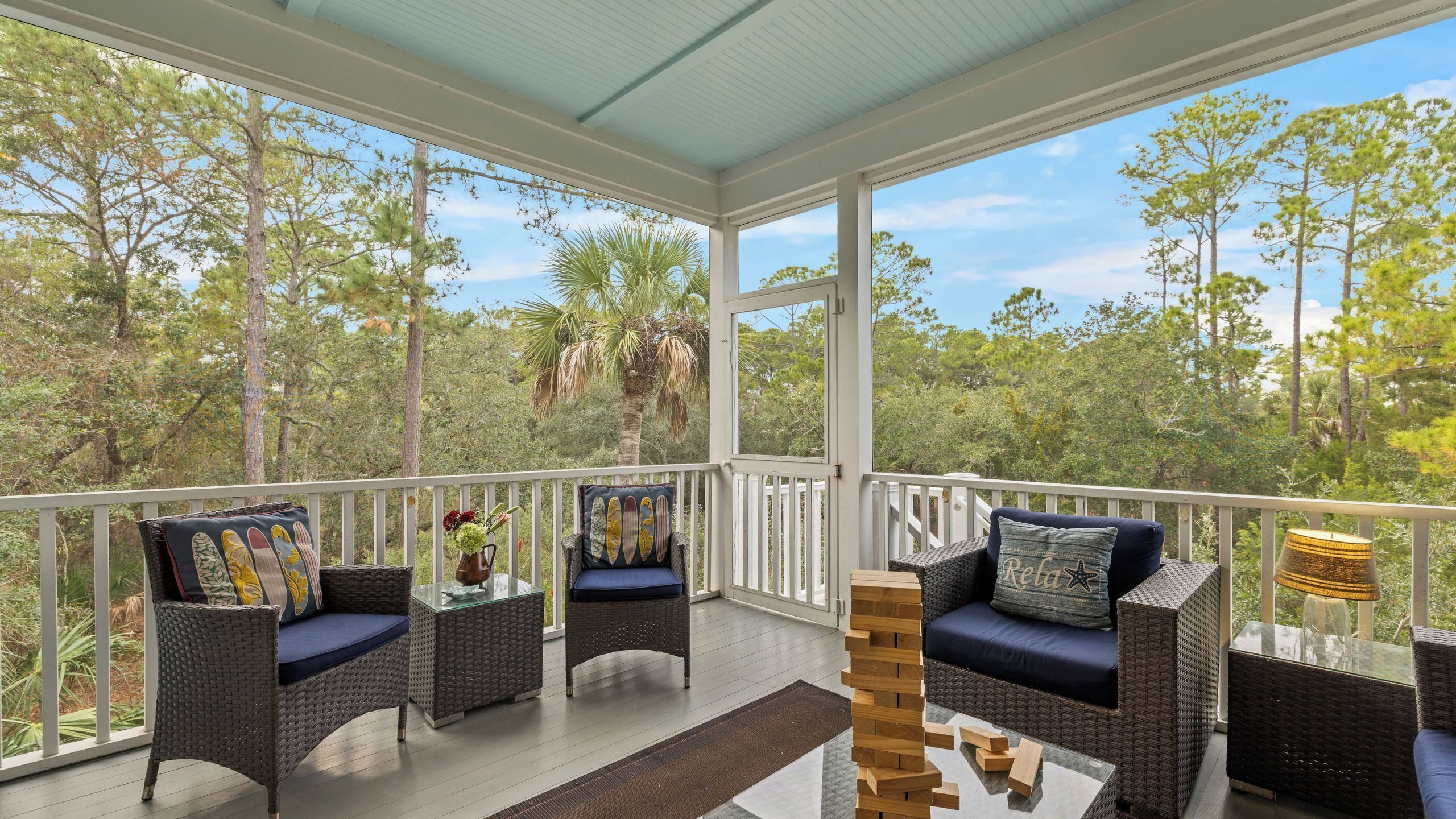 A covered balcony with wicker furniture, a jigsaw puzzle, and a view of a forest.