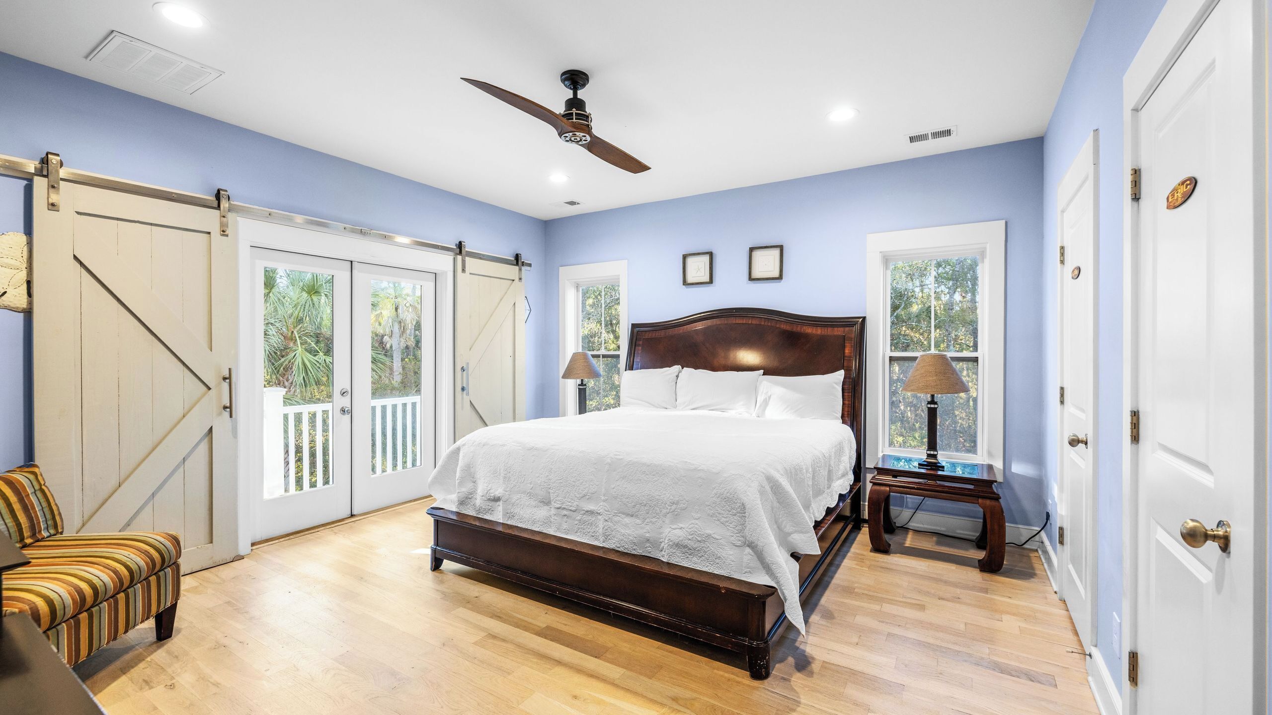 A bedroom with a large bed, a ceiling fan, and a view through a window.