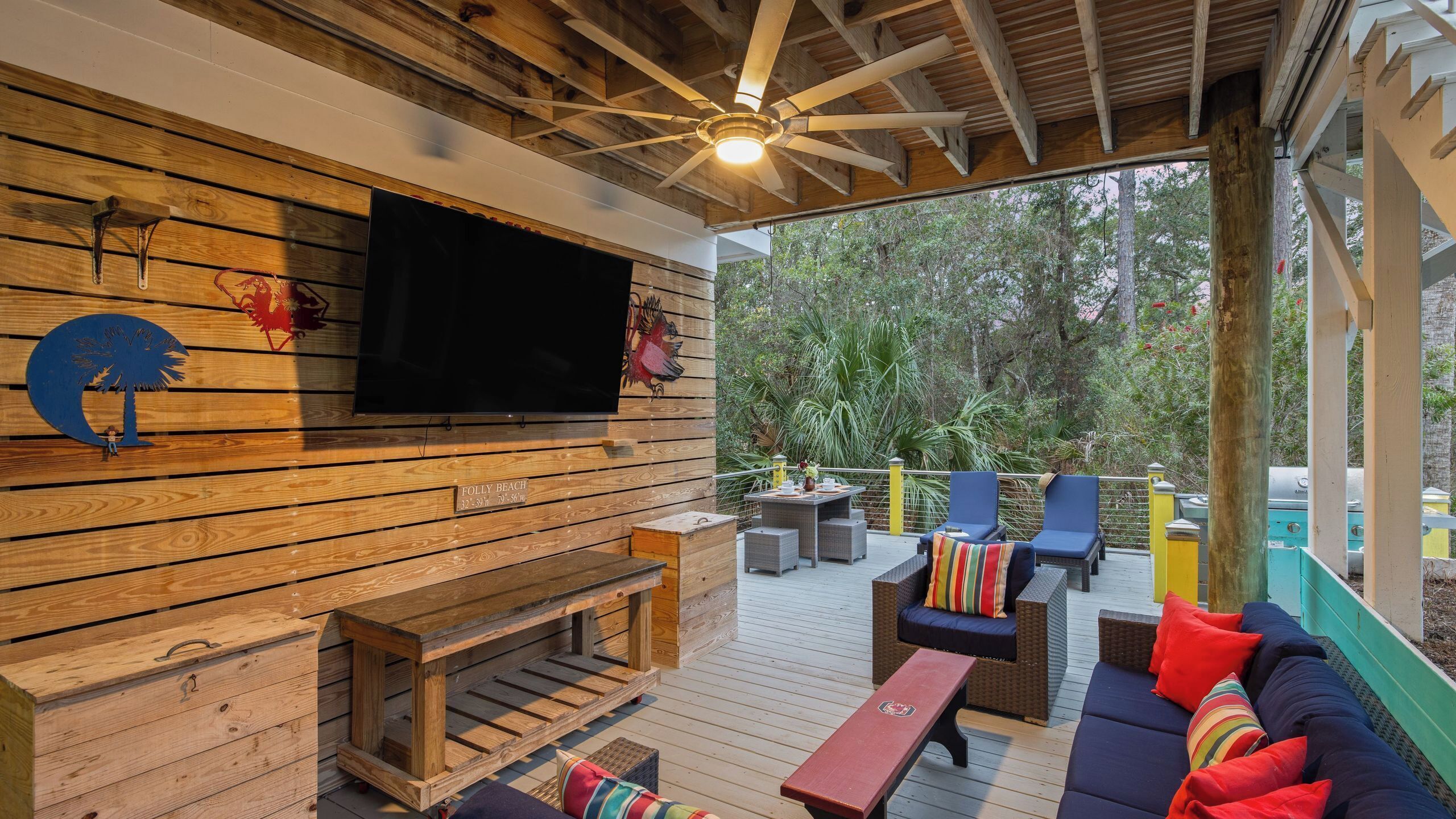 Een houten terras met een televisie, zitplaatsen en een houten wand met een naamplaatje.