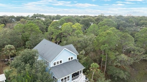 A light blue house surrounded by dense green trees. - Folly Beach Getaway Near Sand Covered Lounge, BBQ & Outdoor TV Tidecrest by Avantstay (Folly Beach)