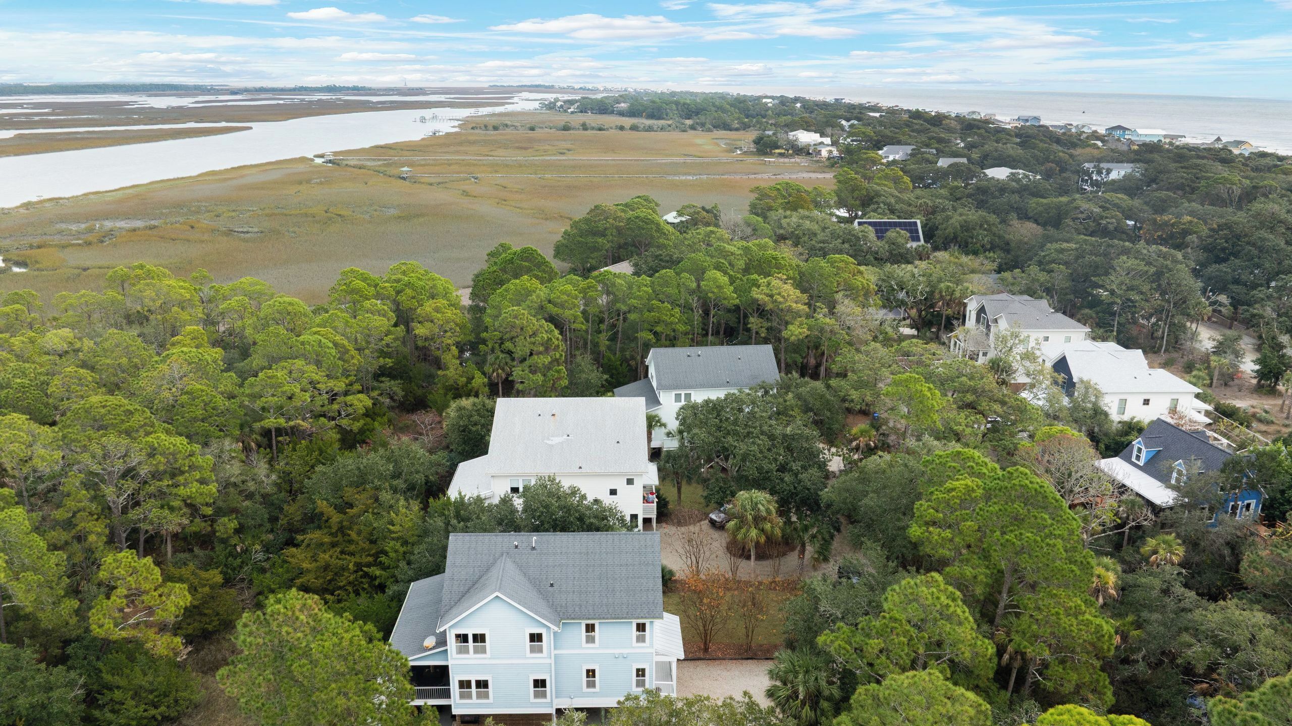 A residential area with houses surrounded by dense trees and a body of water in the background.