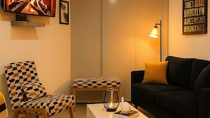 Ein Wohnzimmer mit Kamin, einer Couch, zwei gemusterten Sesseln, einem Couchtisch und einer Lampe.