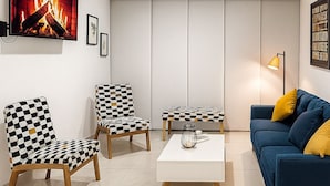 Ein modernes Wohnzimmer mit einer Couch, zwei karierten Sesseln, einem Couchtisch und einem an der Wand montierten Fernseher.