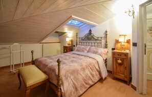 Een slaapkamer met een schuine plafond, dakraam, een bed met versierd hoofdeinde, nachtkastjes met lampen, een bankje en een radiator.