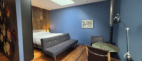 Una habitación con una cama, un sofá, un escritorio y una silla. Cuenta con una lámpara de techo e iluminación de pared.