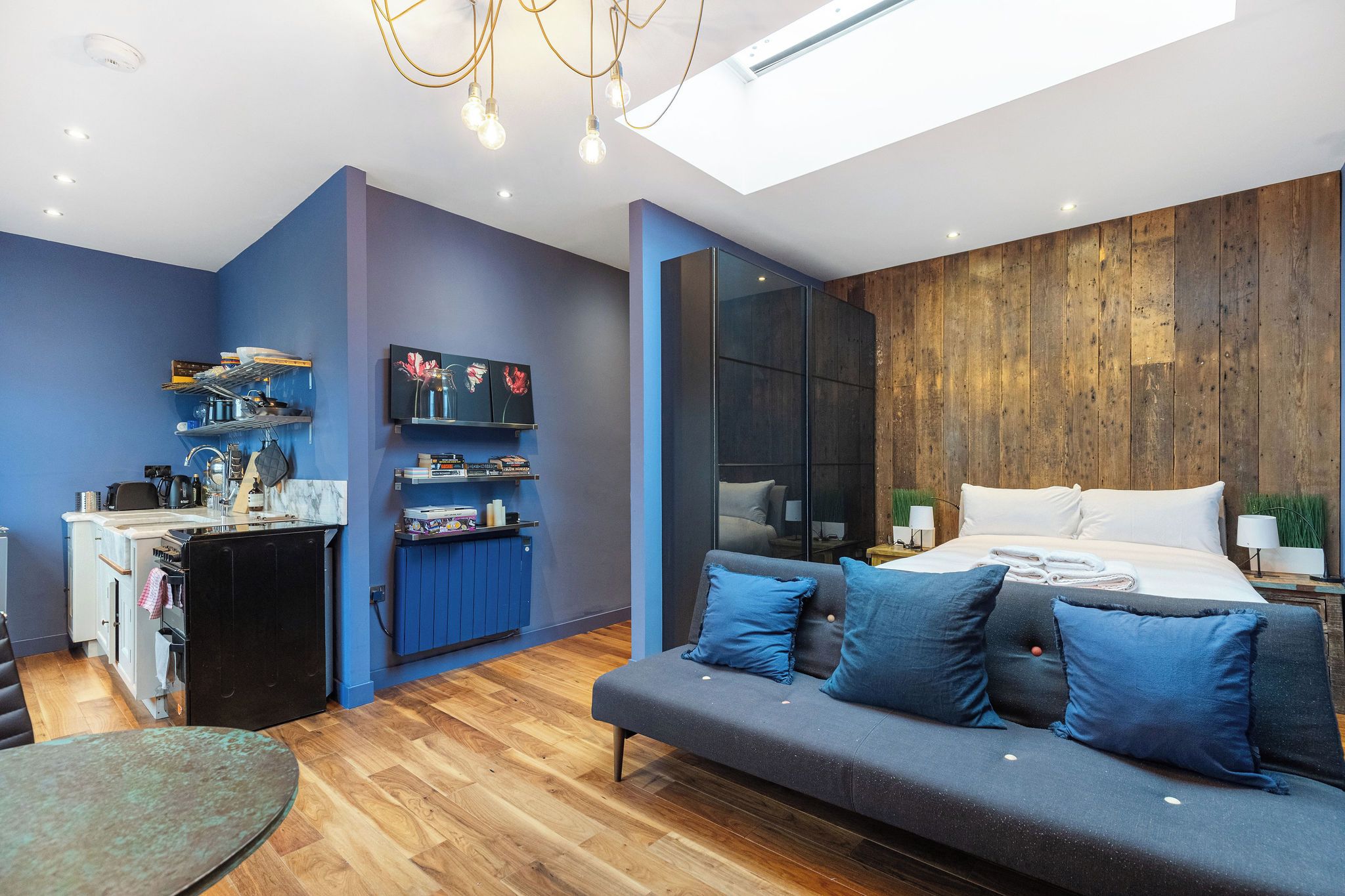 A modern bedroom with a large bed, a sofa, a kitchenette, and a skylight.