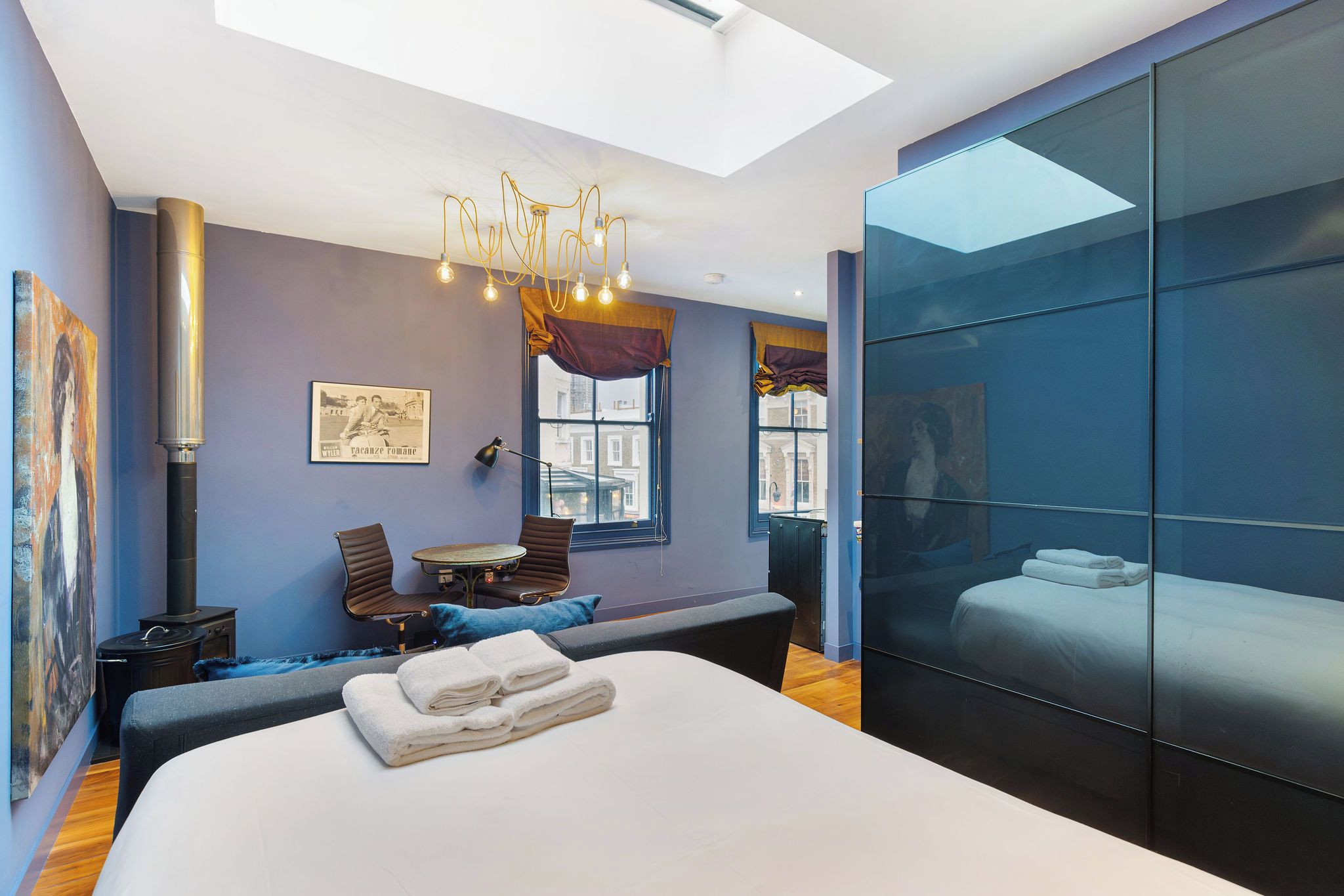 A modern bedroom with a large bed, a seating area with a table, and a large window.