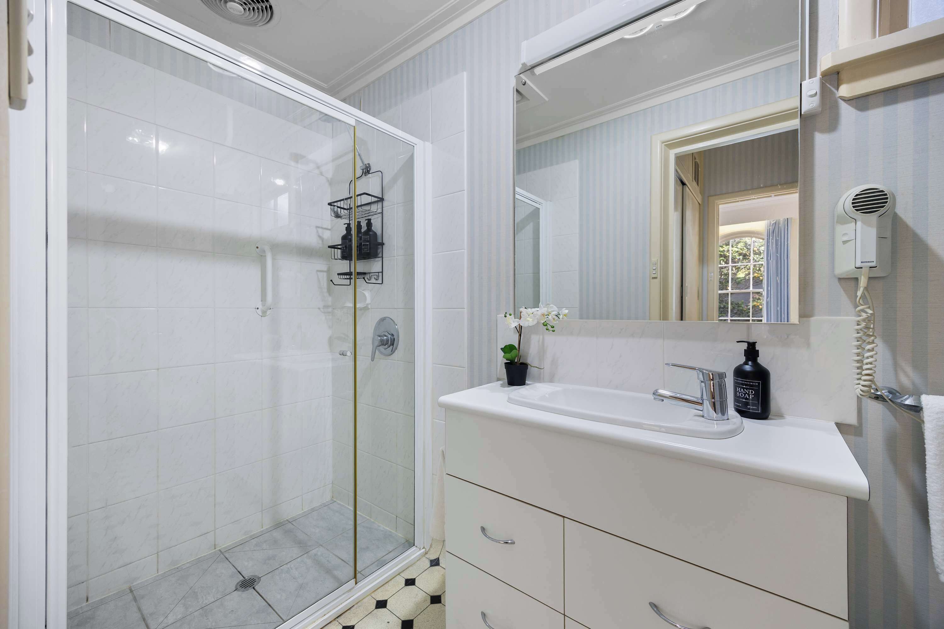 Un bagno con doccia vetro, lavandino bianco con specchio sopra e porta asciugamani.