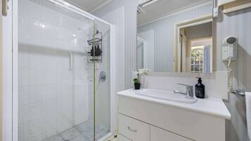 Un bagno con doccia vetro, lavandino bianco con specchio sopra e porta asciugamani.