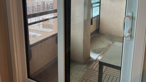 Vista desde un balcón con un paisaje urbano, un pilar de hormigón y una terraza de madera.