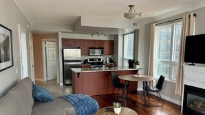 Una sala moderna con sofá, mesa de centro y chimenea. Cuenta con una zona de cocina equipada con refrigerador, microondas y mesa de comedor.