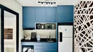 Une cuisine compacte avec des meubles bleus, un four à micro-ondes, une bouilloire et un réfrigérateur.