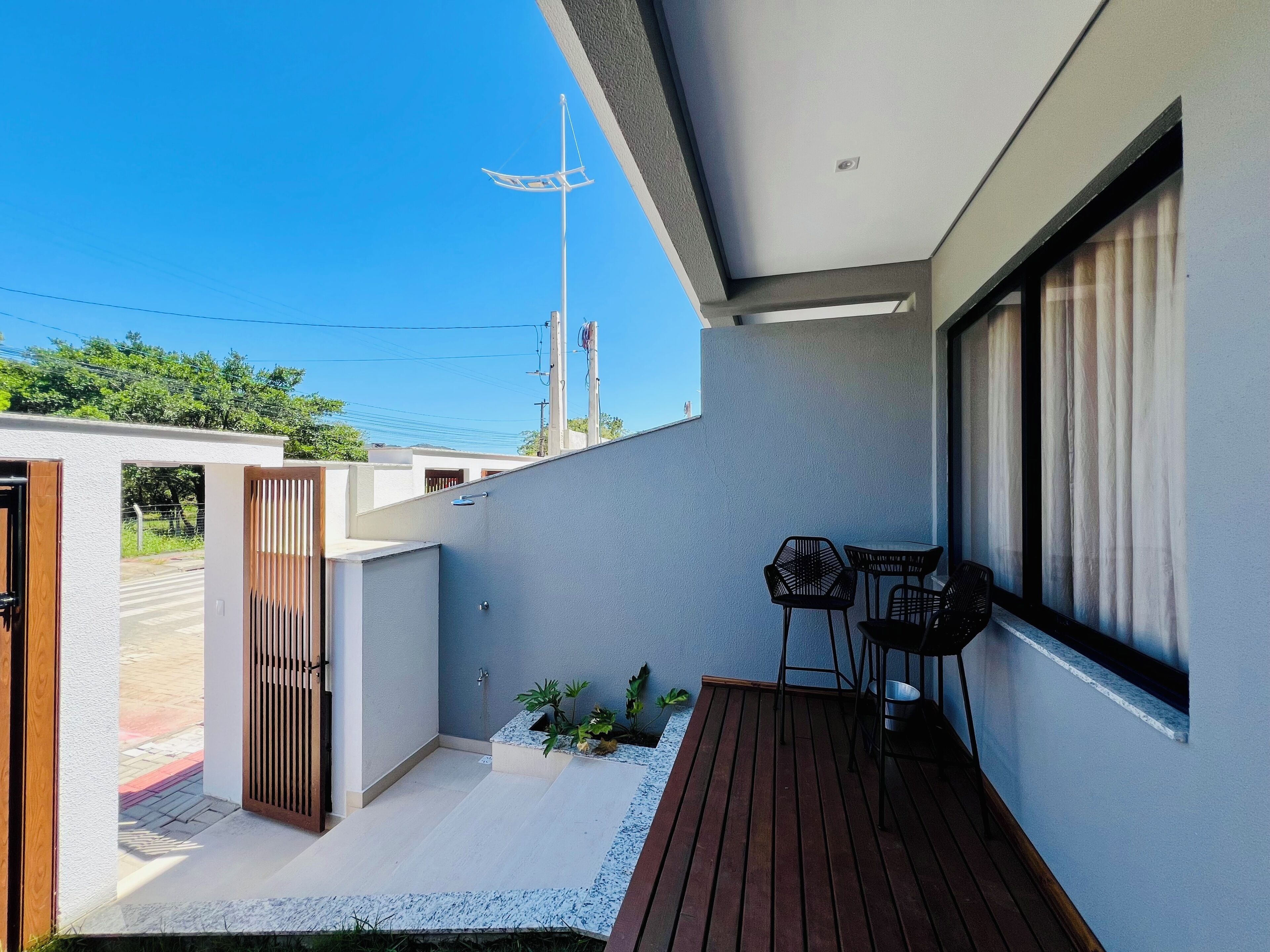 A modern balcony with a wooden floor, a small seating area with two chairs, and a view of the street and power lines in the background.