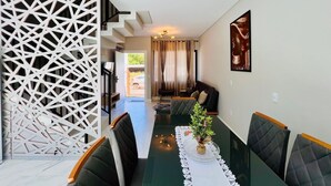Un coin repas avec une table en verre, des chaises à revêtement sombre, une plante décorative en guise de centre de table et un chemin de table blanc en dentelle.