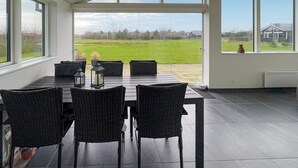 Uma sala de jantar com mesa e cadeiras, grandes janelas e vista para um campo gramado.