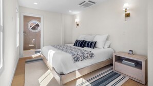 Ein modernes Schlafzimmer mit Bett, Nachttischen und einer Tür zu einem Badezimmer.