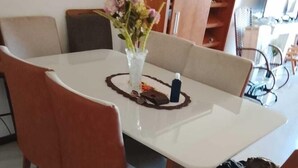 A dining area with a white table, four wooden chairs, and a vase with flowers. - apartamento de temporada  (Uruguaiana)