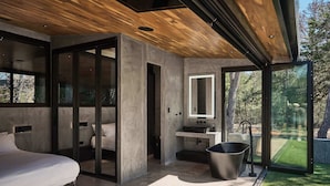Une chambre à coucher moderne, dotée d’un grand lit, d’une douche intégrée et offrant une vue sur une pelouse verdoyante grâce à de grandes fenêtres.