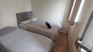 Twee eenpersoonsbedden met gestreepte lakens in een kleine kamer met een houten vloer en een effen muur.