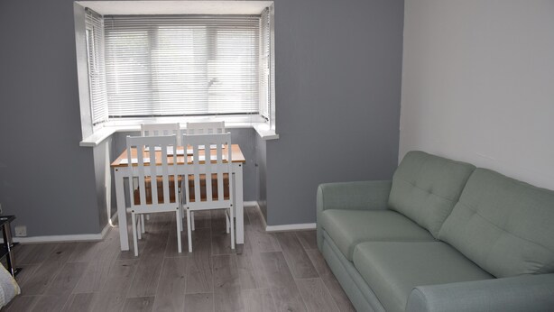 Een kamer met een grijze muur, een houten tafel met een witte stoel en een groene bank.