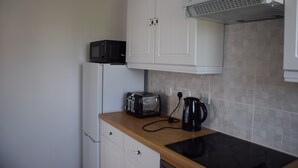 Een keuken met witte kastjes, een magnetron, een broodrooster, een waterkoker en een zwart inductiekookplaat.