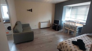 Een kleine, functionele leefruimte met een bank, een tafeltje, een televisie en een wasmachine.
