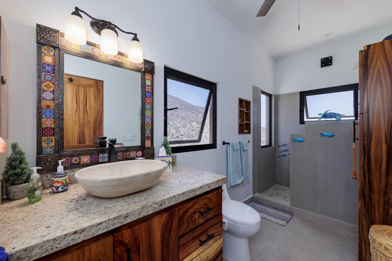 A bathroom with a large mirror, wooden cabinetry, a stone sink, and a view of a mountainous landscape through a window.