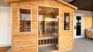 Eine Holzhütte, die als Sauna genutzt wird, mit Glastür und Sitzbank, mit Blick ins Freie.