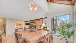 Uma cozinha ampla com uma mesa de jantar de madeira, uma TV fixada na parede e uma janela grande com vista para o exterior.