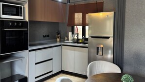 A modern kitchen with a microwave, oven, and refrigerator, wooden cabinets, and a dining area with a table and chairs.