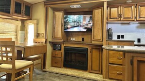 A compact kitchen with wooden cabinets, a built-in TV, a fireplace, and a dining area with a table and chairs. - RV #1 - delightful 1-bdrm, 3 slide out, covered deck, at Lake Livingston Tx  (Onalaska)