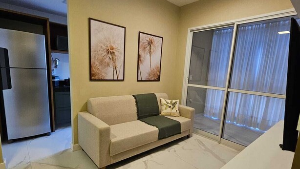 A living room with a sofa, a coffee table, and a large window with curtains. - New apartment one block from the beach with ocean view and garage. (Vila Velha)