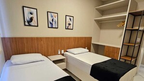 A hotel room with two beds, a wardrobe, and three framed pictures on the wall. - New apartment one block from the beach with ocean view and garage. (Vila Velha)
