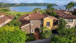A coastal property with stone and tiled roofs, a stone archway entrance, and lush greenery. - Villa Angel 4 bdr Ocean View pool in Los Suenos (Herradura)