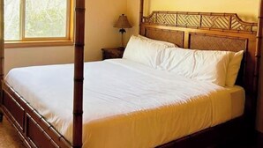 A four-poster bed with a wooden headboard, a window with a view of trees, and a lamp on a bedside table. - Charming Private Suburban Cottage, Serene & Cozy (Mount Vernon)
