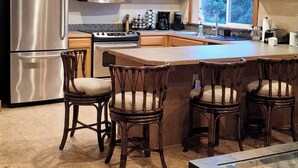 A kitchen with wooden cabinets, stainless steel appliances, and a central island with bar stools. - Charming Private Suburban Cottage, Serene & Cozy (Mount Vernon)