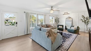 Ein geräumiges Wohnzimmer mit einem hellblauen Sofa, einem dunkelblauen Teppich und einem Deckenventilator.