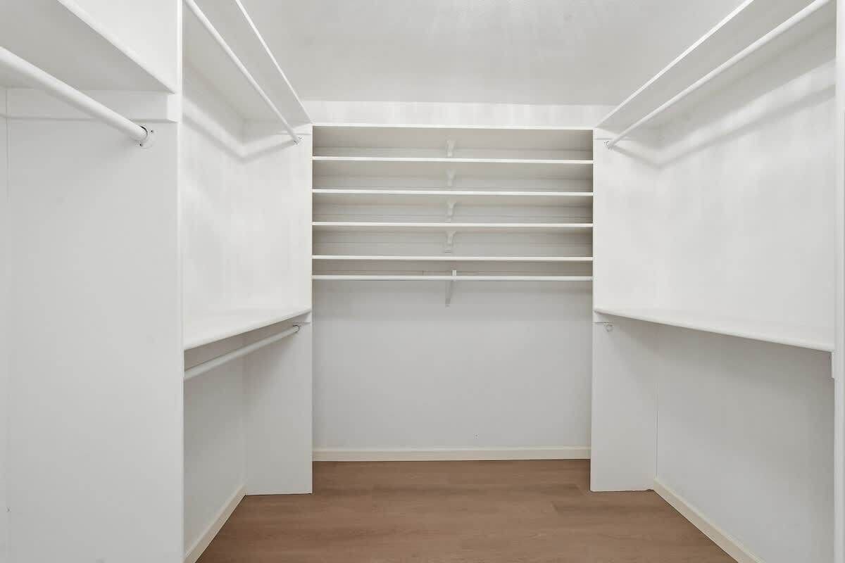 A walk-in closet with white walls and wooden flooring.