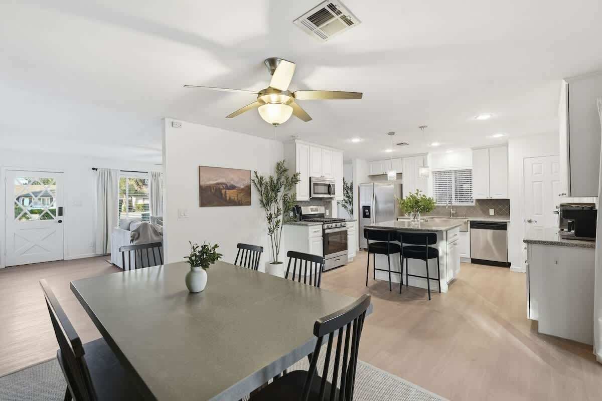 A modern kitchen with white cabinets, a central island, and a dining area with a table and chairs.