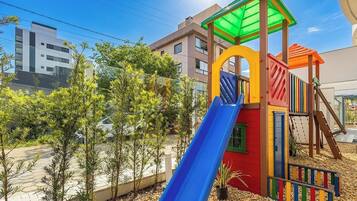 Un parque infantil con un tobogán azul, rodeado de árboles y edificios.