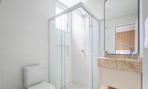 Un baño moderno con cabina de ducha de vidrio, inodoro y lavamanos con espejo.