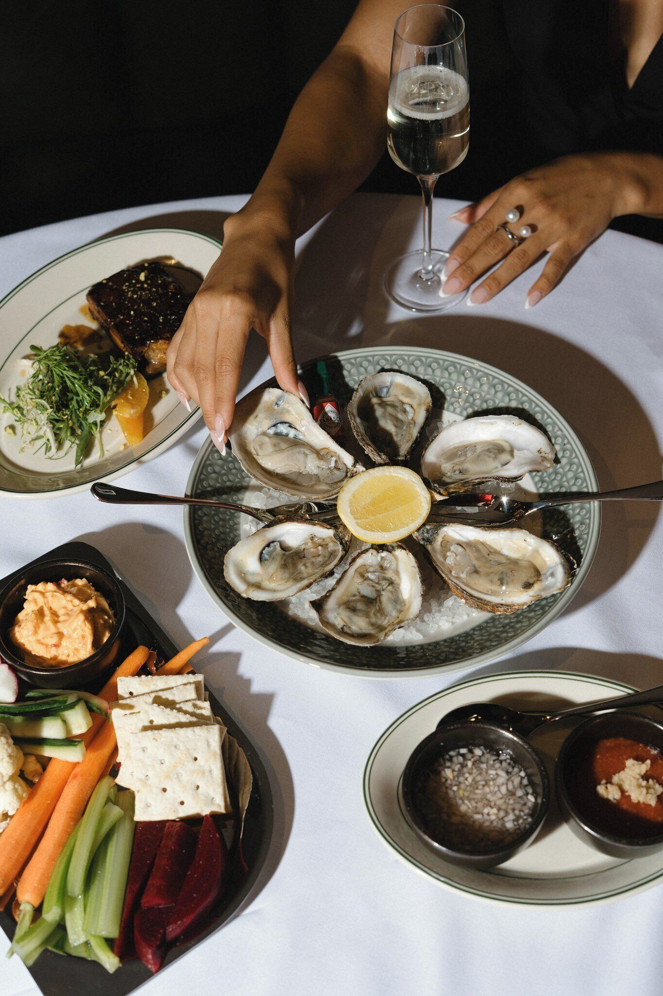 Une table à manger avec une assiette d’huîtres, un verre de vin et divers accompagnements.