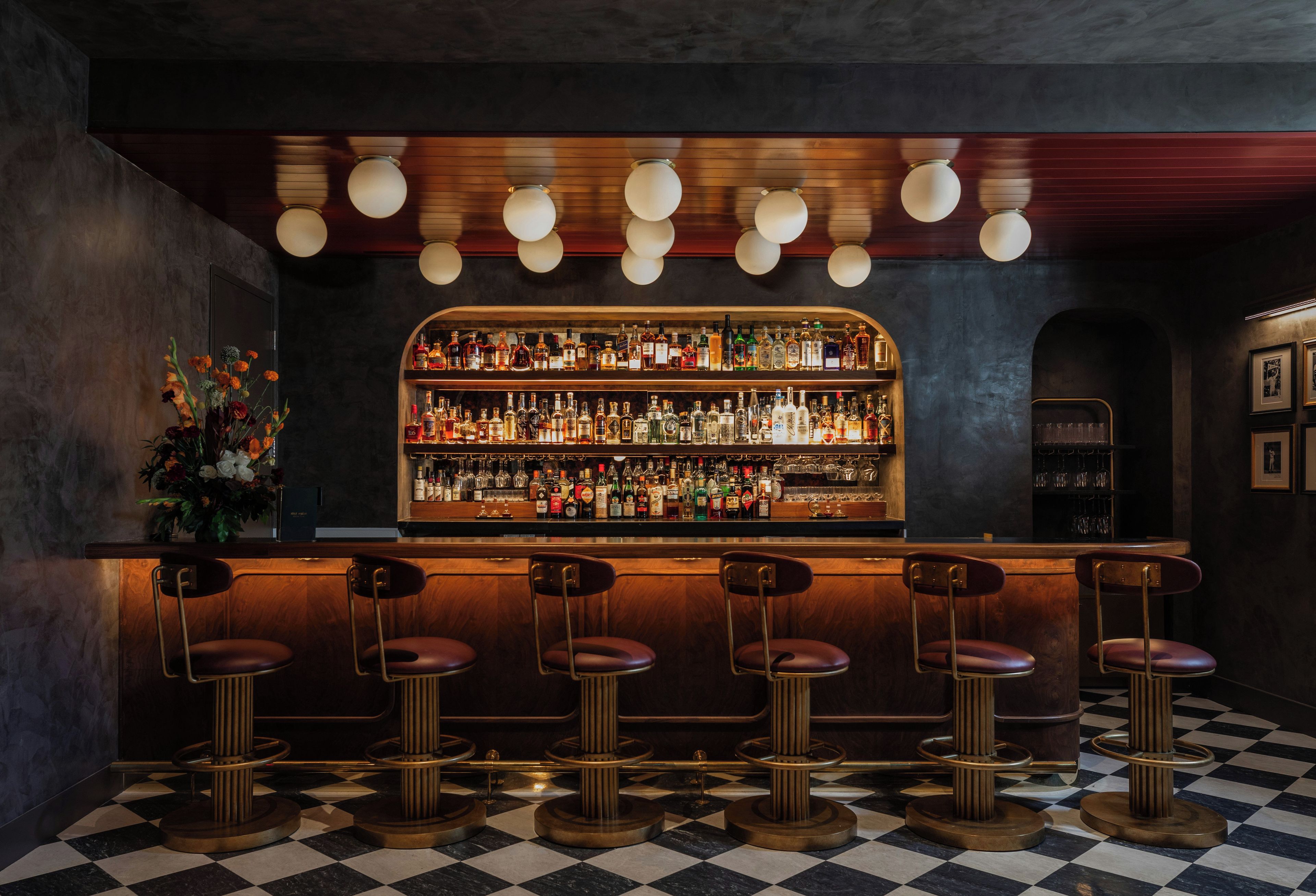A bar with a checkered floor, a variety of bottles, and bar stools.